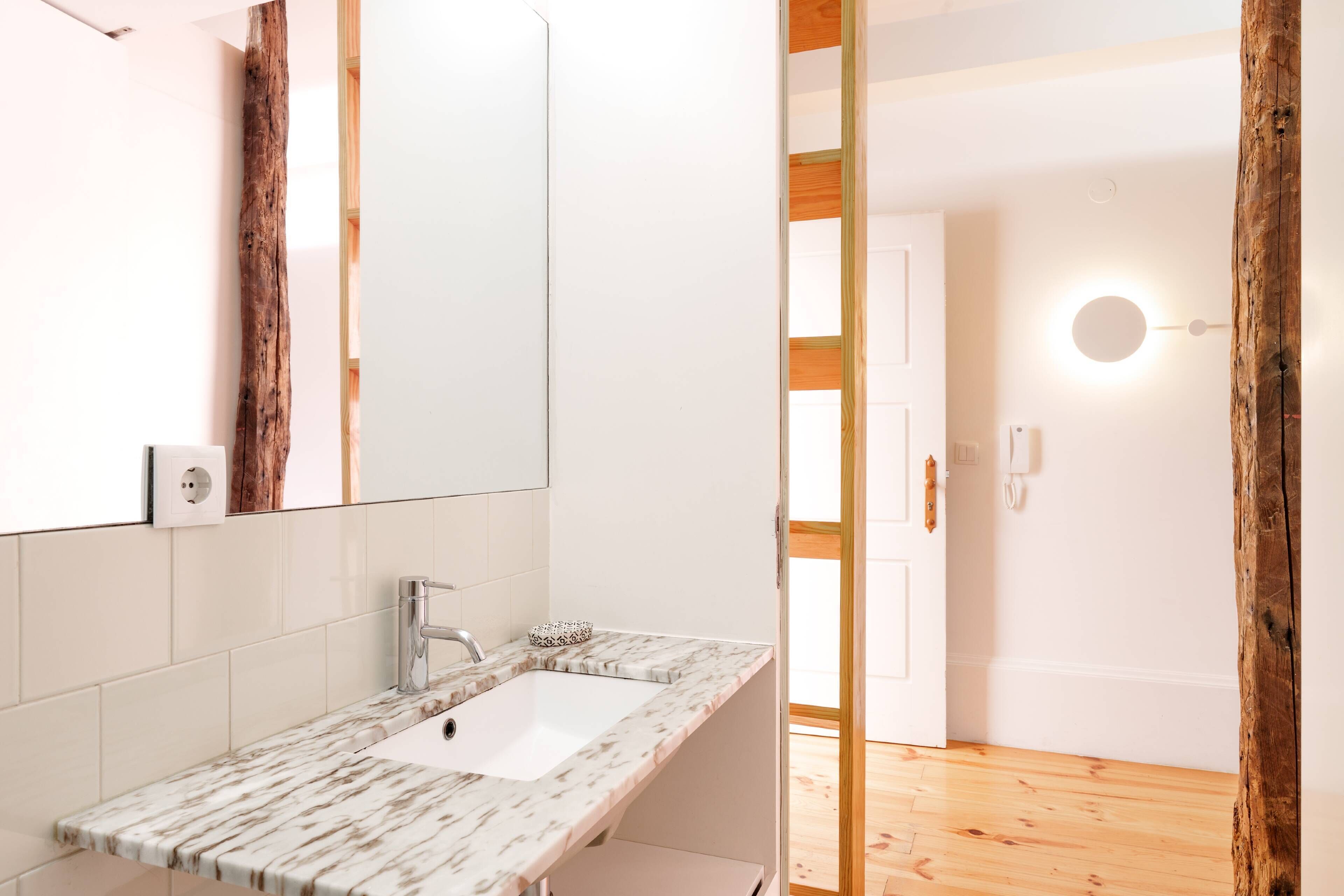 A modern bathroom with a marble sink, a large mirror, and a wooden floor.