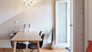 Zona pranzo con tavolo in legno, sedie nere, un lampadario e una porta che dà sull'esterno.