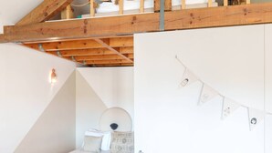 Camera mansarda con soffitto spiovente, travi in legno, un letto a castello, un'armadio bianco e un piccolo comodino.