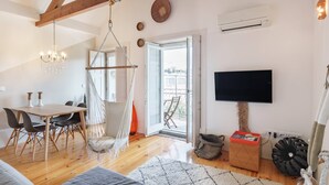 Un'ampia zona giorno con un tavolo da pranzo in legno, una poltrona sospesa, una TV a parete e un'ampia finestra con vista sull'esterno.