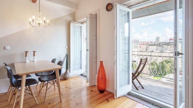 Zona pranzo con tavolo e sedie in legno, un lampadario e un'ampia finestra vista edifici e vegetazione.