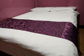 Un letto con una coperta a fiori bianchi e viola, un cuscino bianco e una parete rosa.