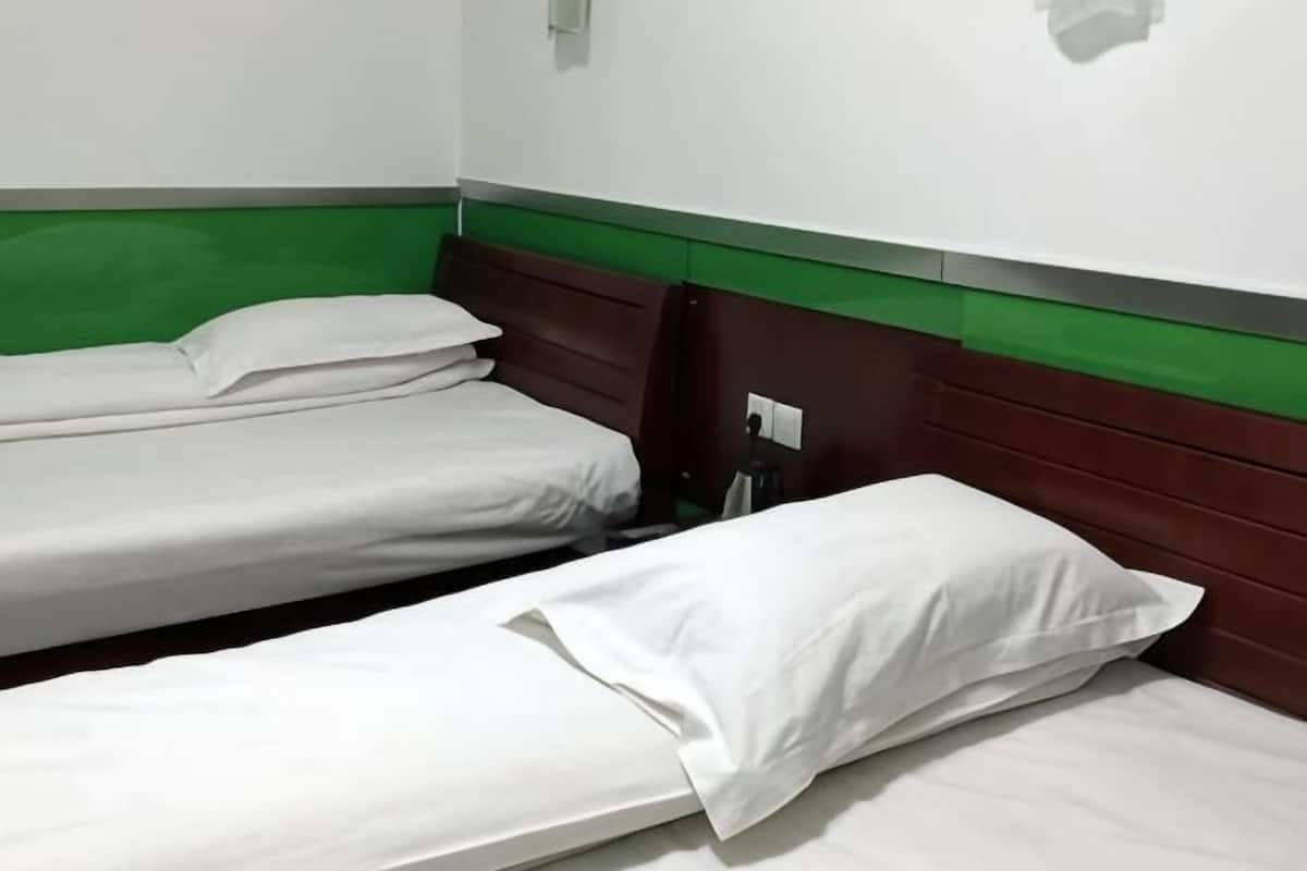 Un lit simple avec une literie blanche, une tête de lit en bois et un mur d’accent vert.