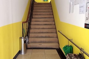 Una escalera con barandilla, un bote de basura y una bolsa verde colgada de la barandilla.