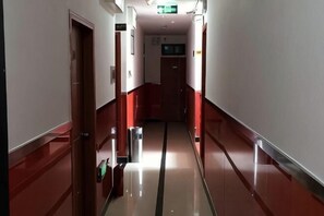 Un corridoio con pavimento lucido, porte su entrambi i lati e un cestino.