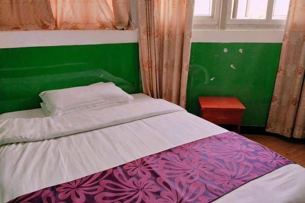 Un lit avec du linge de lit blanc, un mur vert et une fenêtre avec des rideaux.