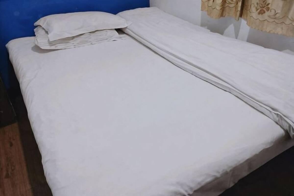 Un lit simple avec une literie blanche, une tête de lit bleue et un rideau beige.