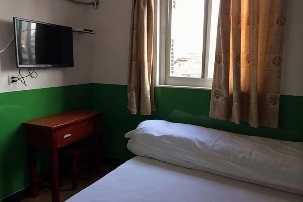 Ein Zimmer mit einem Bett, einem Schreibtisch, einem Fernseher und einem Fenster mit Vorhängen.