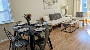 Ein modernes Wohnzimmer mit Essbereich, ausgestattet mit einer Couch, einem Couchtisch und einem Esstisch für vier Personen.
