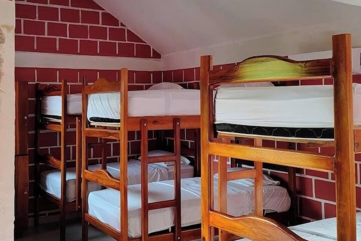 A dormitory room with bunk beds arranged in two rows, a red brick wall, and a white ceiling.