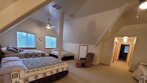 A spacious attic bedroom with two beds, a chair, and a door leading to another room. - Charming 3-bedroom house in the beautiful mountains of Pine, Idaho. (Mountain Home)