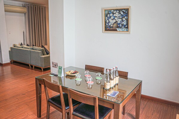 A dining area with a glass table, wooden chairs, and a painting on the wall.