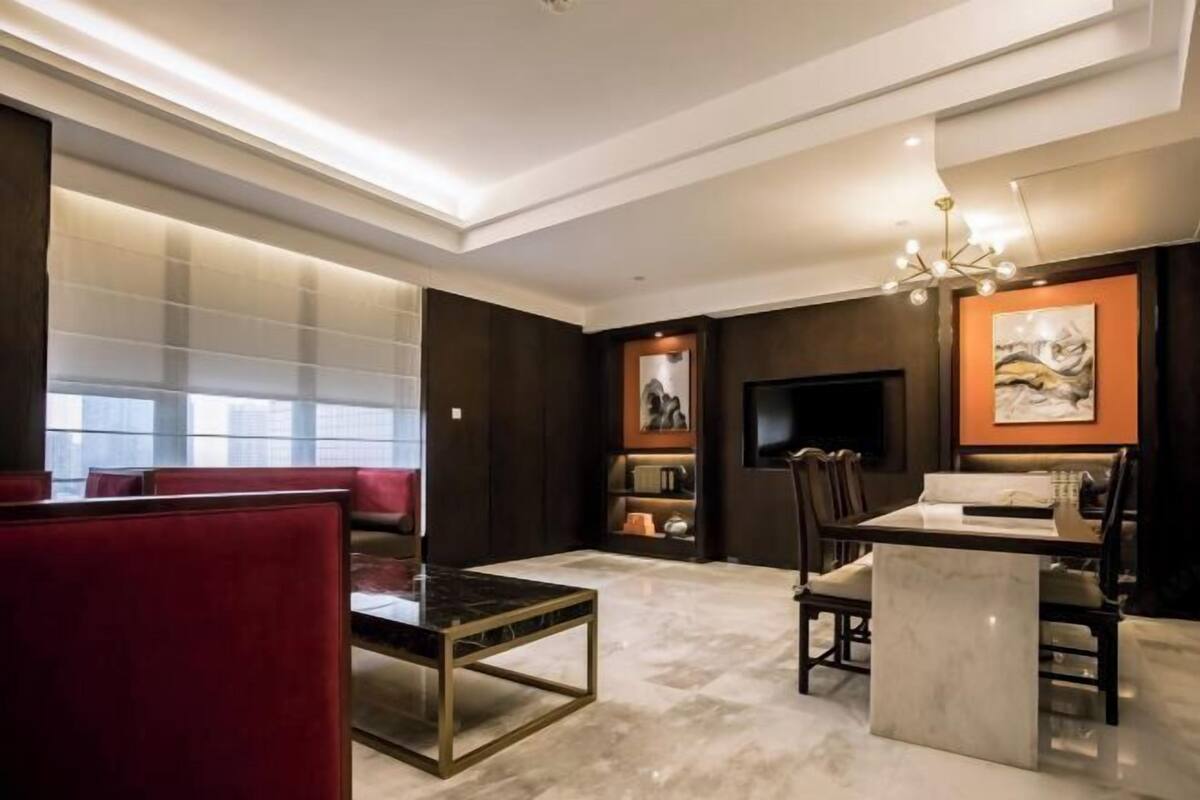 A modern living room with a glass partition, a red sofa, a dining table, and a TV.