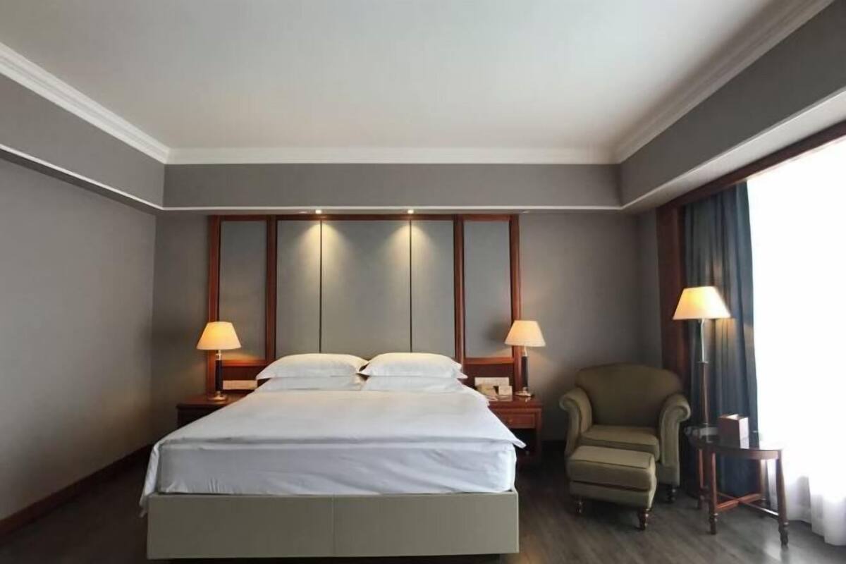 A hotel room with a large bed, two bedside tables with lamps, a chair, and a window with curtains.