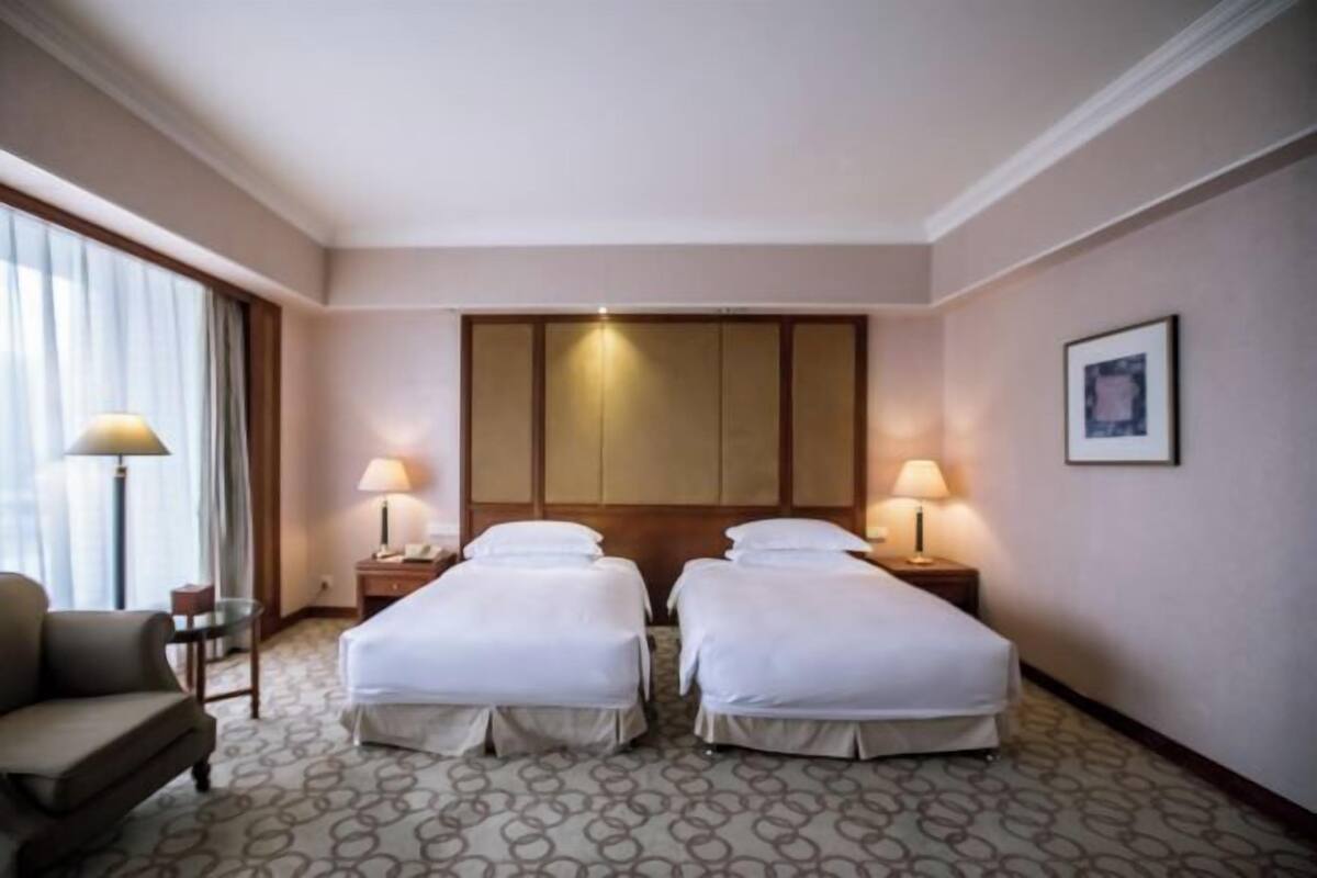 A hotel room with two beds, a chair, a desk, and a lamp.