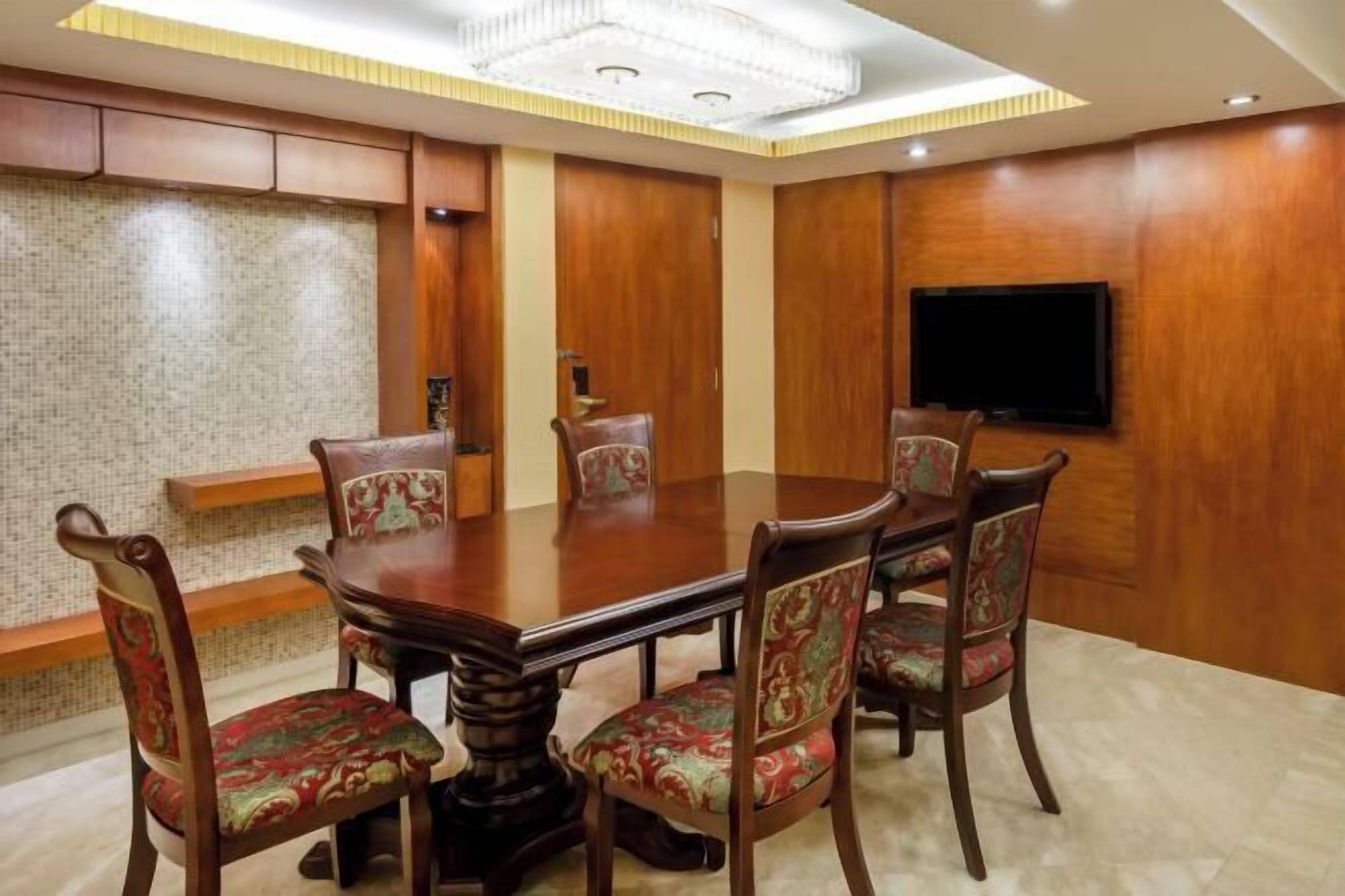 A conference room with a wooden table and chairs, a flat-screen TV mounted on the wall, and a patterned wall.