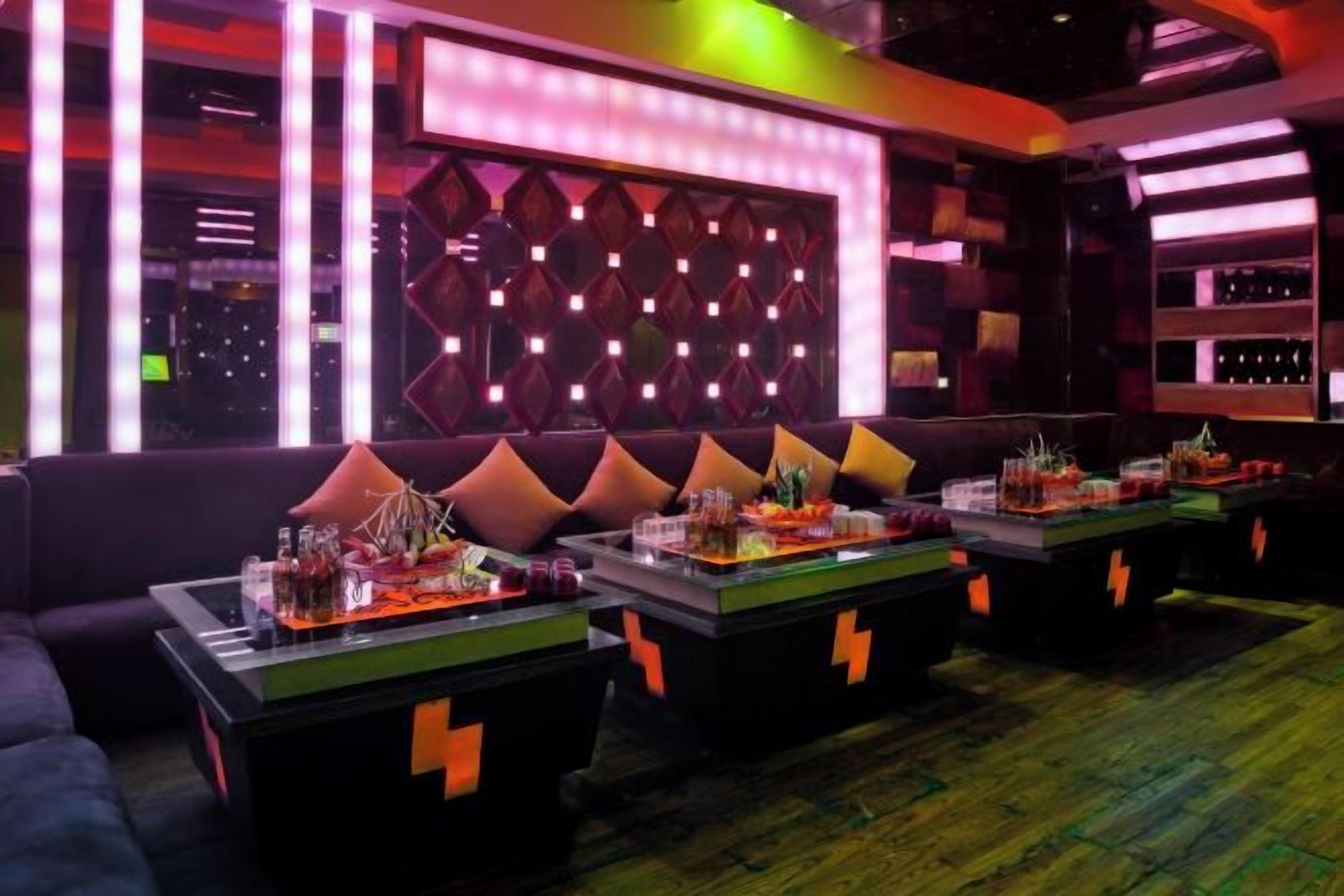 Eine moderne Lounge mit einem dunkelgrauen Sofa, mehreren Tischen mit Dekoration und einer Wand mit beleuchteten Elementen.