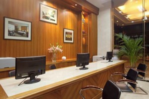 A reception desk with two monitors, framed pictures on the wall, and a potted plant. - Zhanjiang Shanhe Hotel (Zhanjiang)