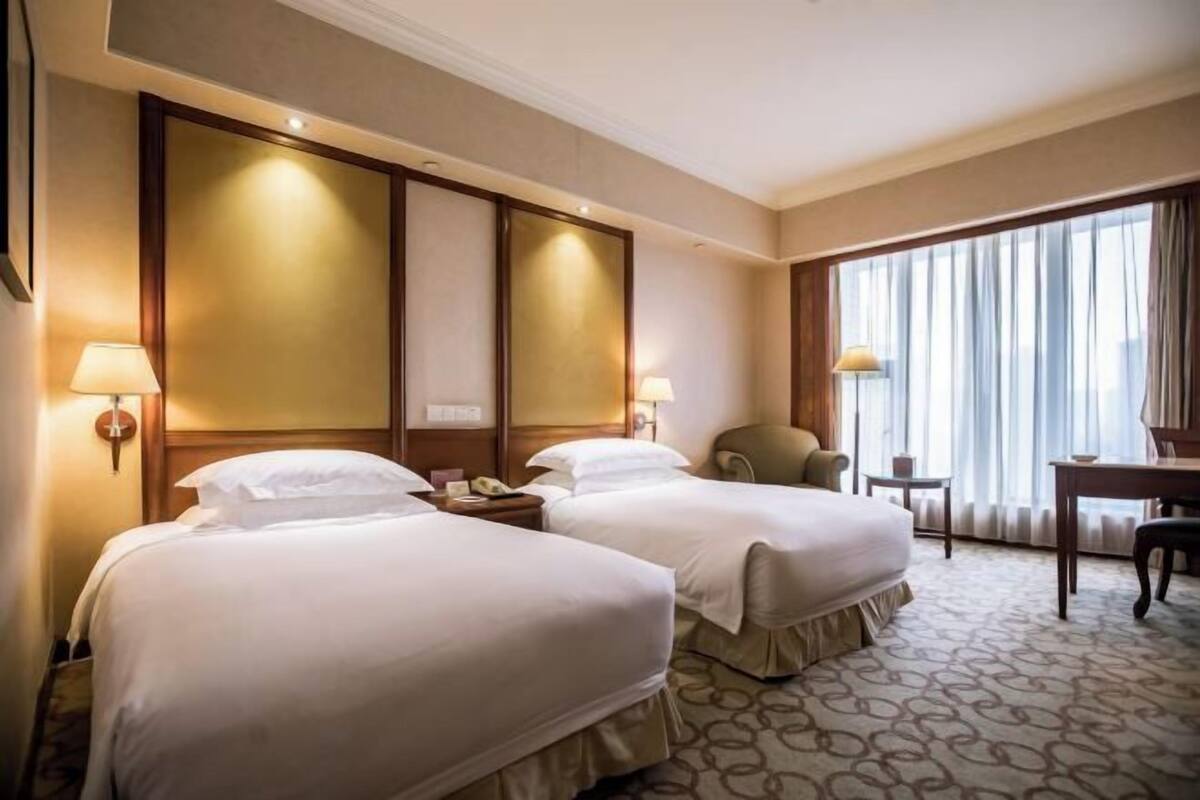 A hotel room with two beds, a desk, a chair, and a large window with curtains.