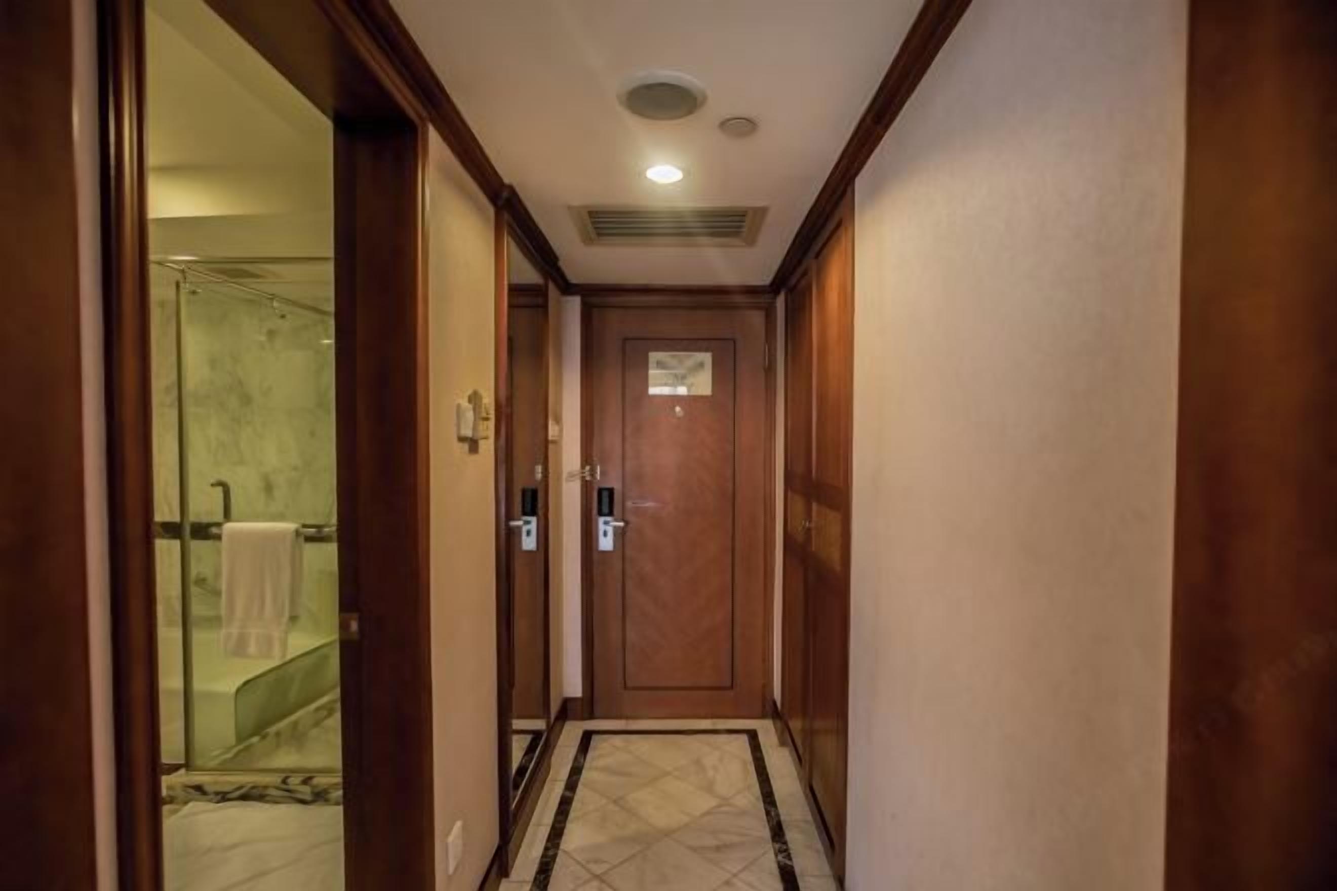 A hallway with a wooden door, a glass shower area, and a tiled floor.