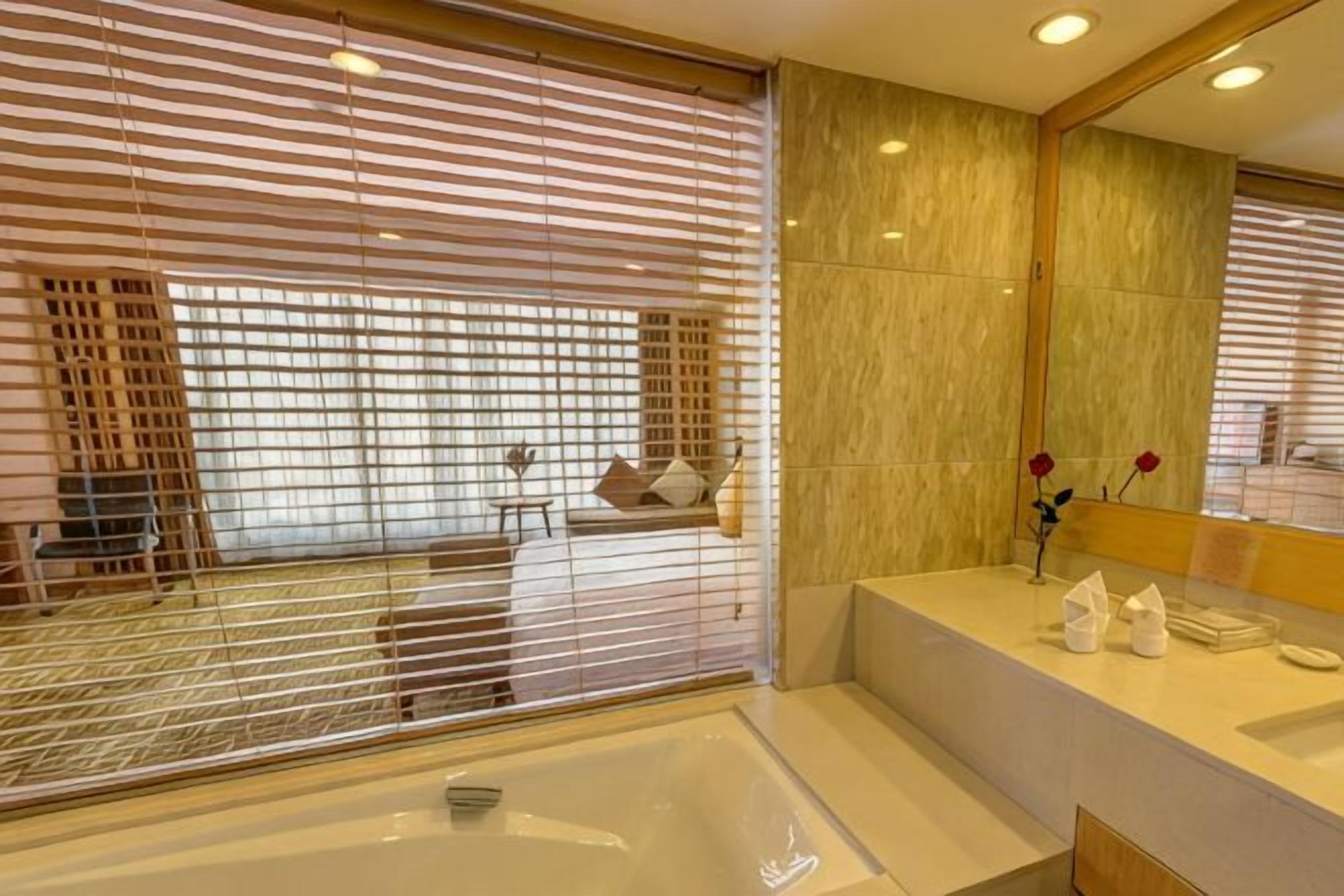 Un baño moderno con bañera, tocador con espejo y ventana con persianas.