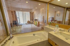 A modern bathroom with a large bathtub, a vanity with a mirror, and a view through a window with blinds. - Zhanjiang Shanhe Hotel (Zhanjiang)