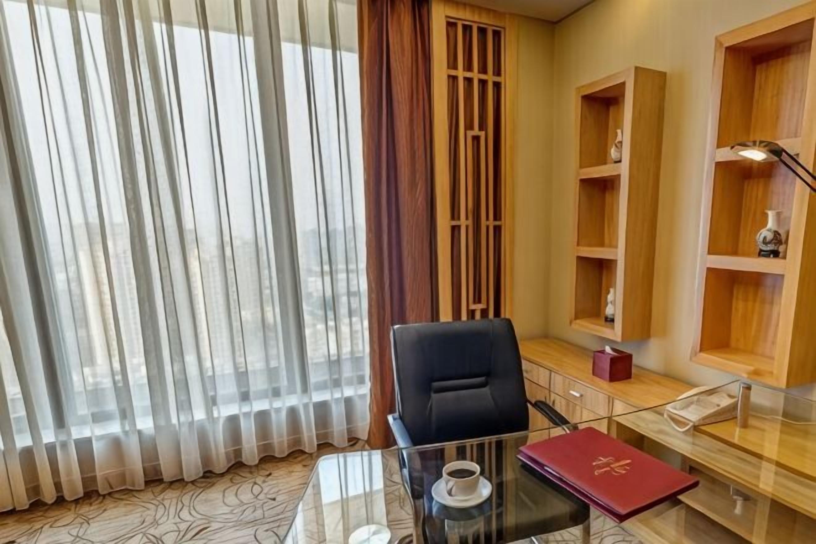 Une pièce avec une table en verre, une chaise, un livre rouge et des étagères en bois ornées d’objets décoratifs.
