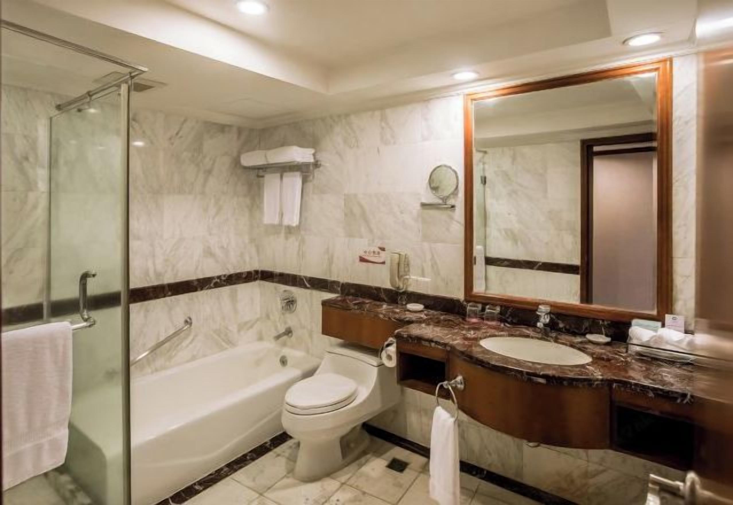 Ein modernes Badezimmer mit Duschkabine aus Glas, einer Badewanne, einer Toilette und einem Waschtisch mit Waschbecken und Spiegel.