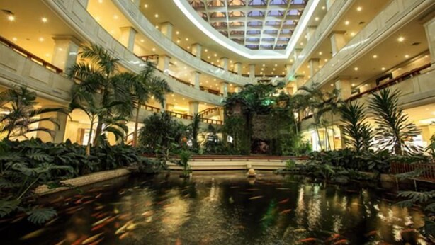 A spacious atrium with a central water feature, surrounded by lush greenery and a high ceiling with skylights. - Zhanjiang Shanhe Hotel (Zhanjiang)