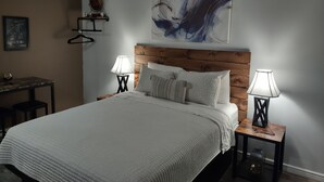 Een slaapkamer met een groot bed, twee nachtkastjes met lampen, een houten hoofdbord, een wandplank met een decoratief object en een ingelijst schilderij aan de muur.