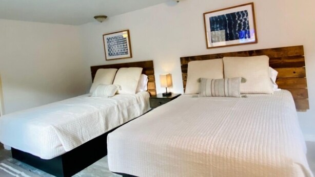 Een hotelkamer met twee bedden, elk voorzien van een houten hoofdbord, wit beddengoed en een klein nachtkastje met een lamp.