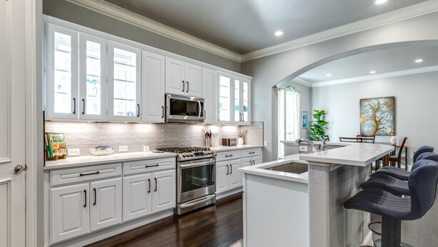 A modern kitchen with white cabinets, stainless steel appliances, and a bar area with stools.