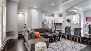 A spacious living room with a grey sectional sofa, ottoman, and matching chairs, a coffee table, and a patterned rug.