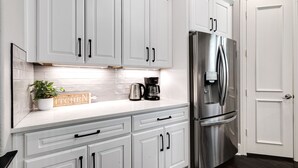 A modern kitchen with white cabinets, a stainless steel refrigerator, and a coffee maker on the counter.