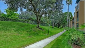 A pathway leading through a well-maintained grassy area with trees and a building on the right.