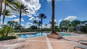 A pool area with palm trees, lounge chairs, and a clear blue sky.
