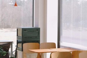 A room with a table and chairs, a window with blinds, and a green cabinet. - 7 Days Hotel (Penglaige Street Dengzhou Road Market Branch, Penglai)‌ (Yantai)