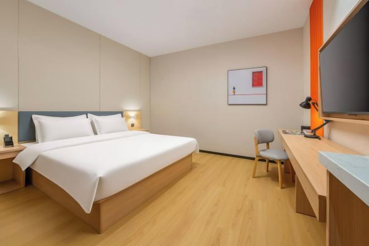 A hotel room with a large bed, a desk, a chair, and a flat-screen TV.
