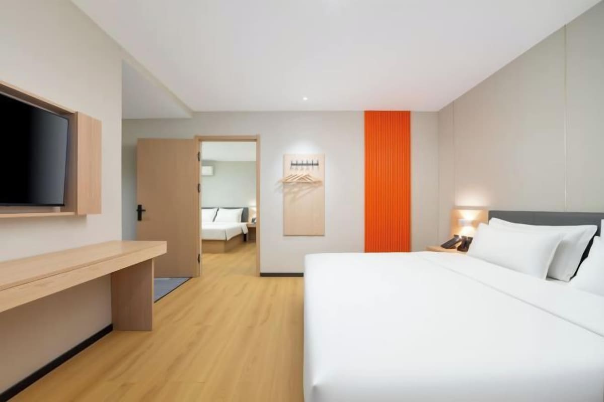 A hotel room with a bed, a TV, a desk, and a door leading to another room.