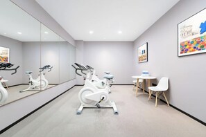 A modern gym with stationary bikes, a mirrored wall, and a small table with chairs. - 7 Days Hotel (Penglaige Street Dengzhou Road Market Branch, Penglai)‌ (Yantai)