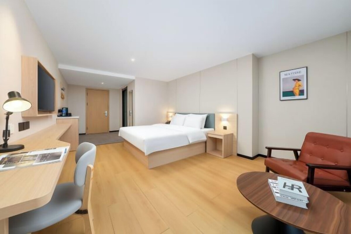 A hotel room with a bed, bedside tables, a desk, a chair, and a small table with a sign.