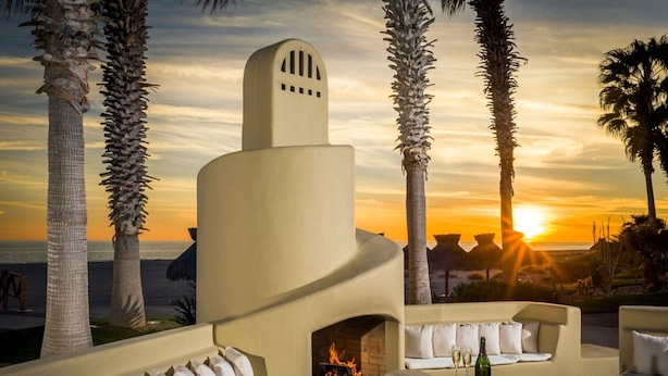 Un área de descanso al aire libre, moderna, con chimenea, asientos y vistas al atardecer sobre el océano.