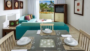 Un área de comedor con una mesa dispuesta para cuatro personas, un sofá color turquesa, un televisor y cuadros en las paredes.