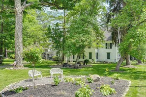 A well-maintained garden with a white bench, a small tree, and a house in the background. - New Studio Walkable to Lake & Village w/ Pool! (Hammondsport)