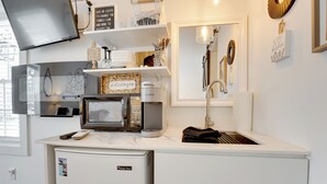 Een moderne keuken met een ingebouwde magnetron, koffiezetapparaat en een spoelbak. Er zijn planken met keukengerei en een kleine koelkast.
