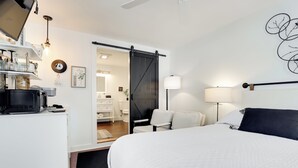 Een moderne hotelkamer met een groot bed, een bureau met een magnetron, een schuifdeur naar de badkamer en een wandlamp.