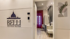 Un couloir avec une enseigne indiquant « Belli Vatican Suites », et un intérieur moderne comprenant un bureau et une chaise.