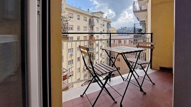A balcony with a table and chairs, overlooking a row of apartment buildings.