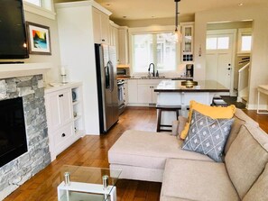 A modern kitchen with a stone fireplace, white cabinetry, and a central island.