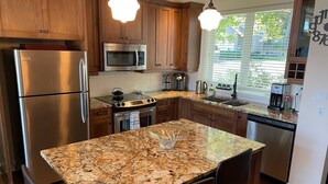 A modern kitchen with granite countertops, stainless steel appliances, wooden cabinets, and pendant lighting.